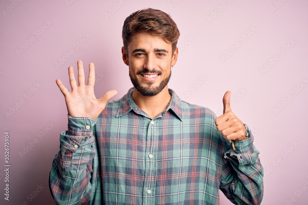 Young handsome man with beard wearing casual shirt standing over pink background showing and pointing up with fingers number six while smiling confident and happy. Young handsome man with beard wearing casual shirt standing over pink background showing and pointing up with fingers number six while smiling confident and happy.