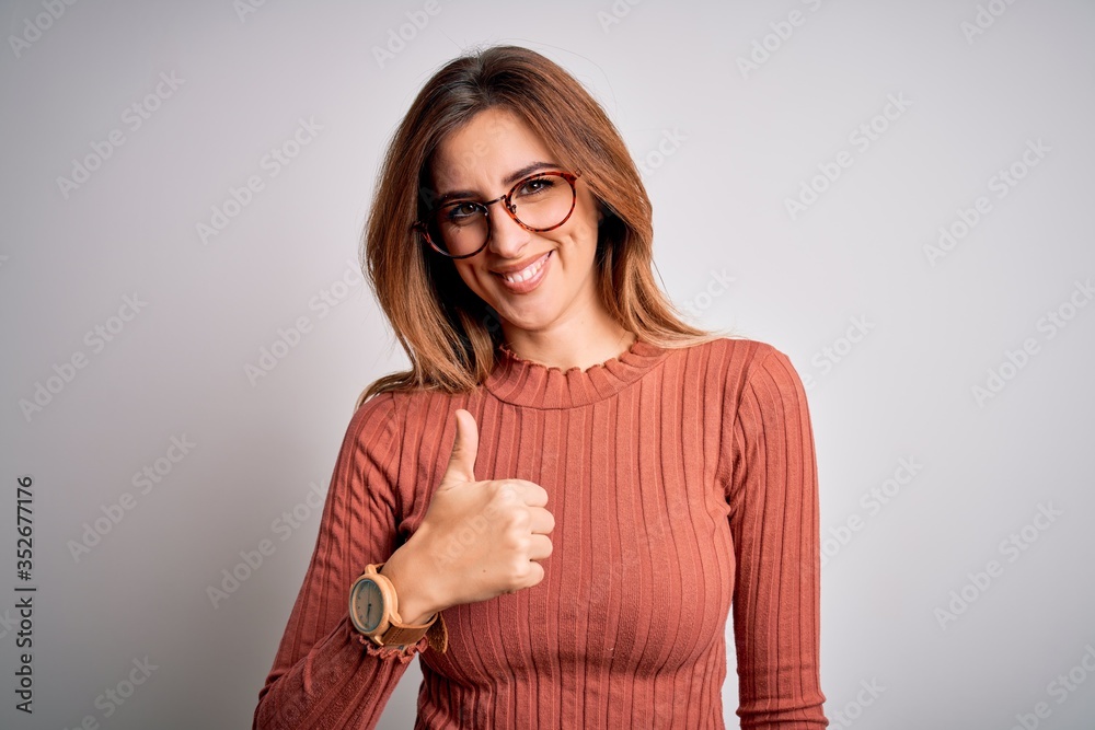 Young beautiful brunette woman wearing casual sweater and glasses over white background doing happy thumbs up gesture with hand. Approving expression looking at the camera showing success. Young beautiful brunette woman wearing casual sweater and glasses over white background doing happy thumbs up gesture with hand. Approving expression looking at the camera showing success.