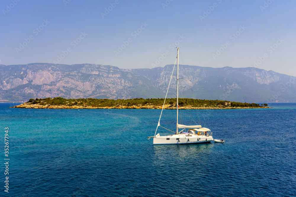 White small sailing yacht in the Aegean. Small island on a background of mountains