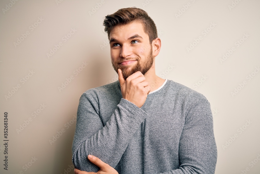 Young handsome blond man with beard and blue eyes wearing casual sweater with hand on chin thinking about question, pensive expression. Smiling with thoughtful face. Doubt concept. Young handsome blond man with beard and blue eyes wearing casual sweater with hand on chin thinking about question, pensive expression. Smiling with thoughtful face. Doubt concept.