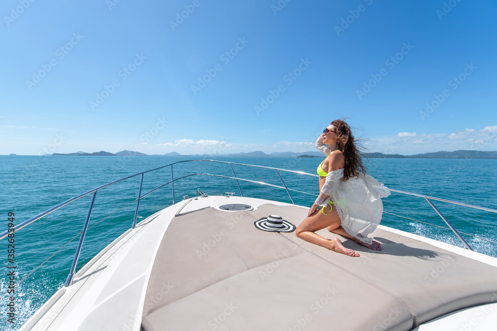Fashion photo of adorable young woman sitting on edge of luxury yacht and looking for the sea during sailing trip. Happy woman enjoying summer travel. Vacation concept