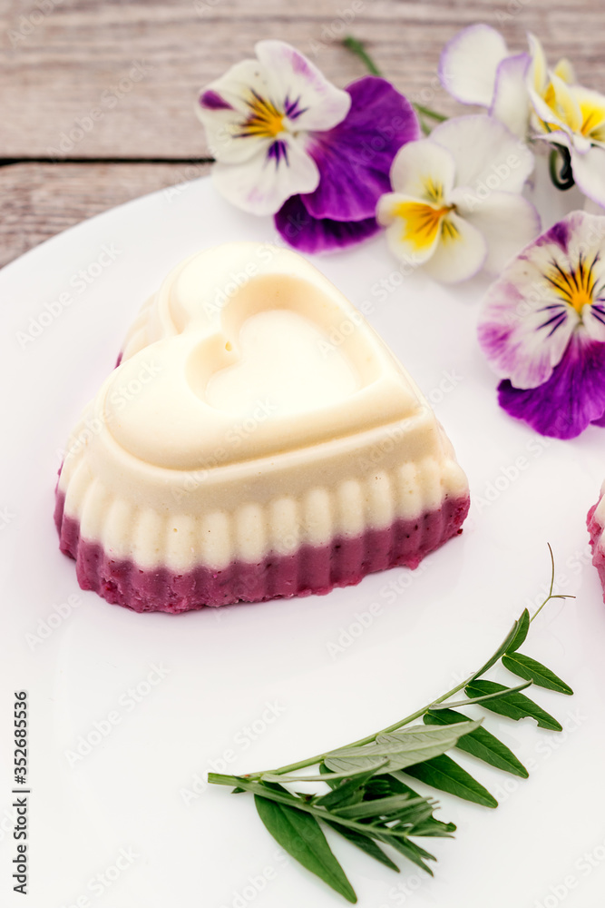 Souffle in the shape of a heart with cottage cheese, agar-agar and cream on a white plate on a wooden background.Edible flowers adorn the composition.Сoncept of healthy food and healthy dessert Souffle in the shape of a heart with cottage cheese, agar-agar and cream on a white plate on a wooden background.Edible flowers adorn the composition.Сoncept of healthy food and healthy dessert