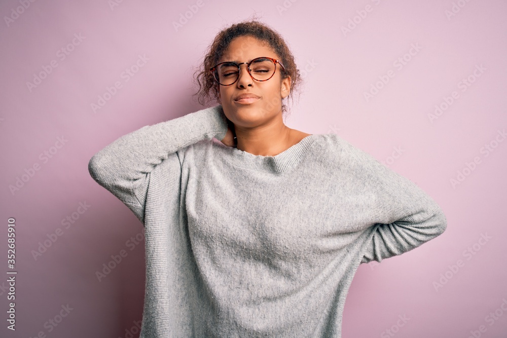 Young beautiful african american girl wearing sweater and glasses over pink background Suffering of neck ache injury, touching neck with hand, muscular pain Young beautiful african american girl wearing sweater and glasses over pink background Suffering of neck ache injury, touching neck with hand, muscular pain