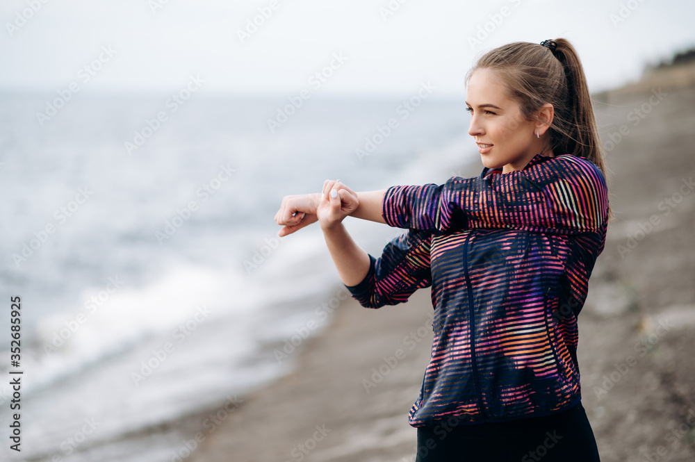 Warming up before workout. Young athletic girl in sportswear is warming up before jogging outdoors near the sea. She stretches the whole body before workout Warming up before workout. Young athletic girl in sportswear is warming up before jogging outdoors near the sea. She stretches the whole body before workout