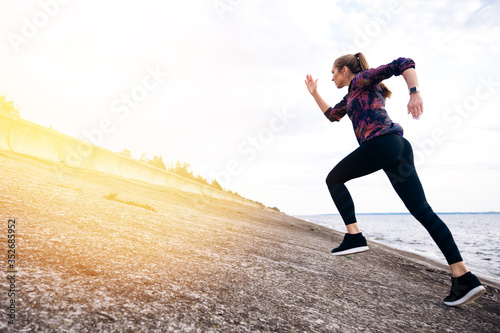 Jogging outdoors. Cardio workout. Young attractive athletic girl in sportswear is jogging outdoor near the sea