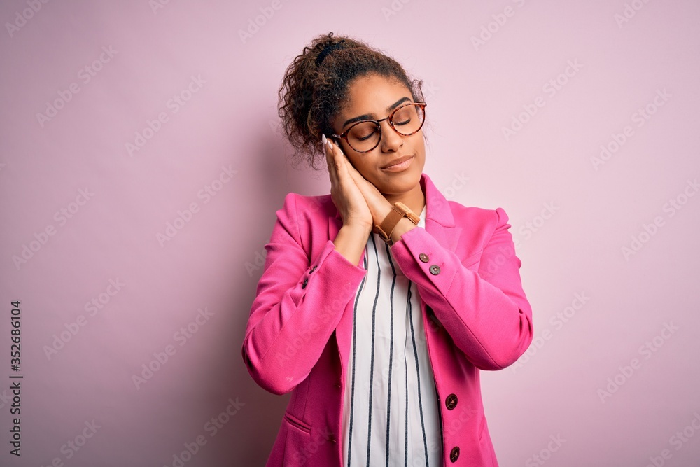 Beautiful african american businesswoman wearing jacket and glasses over pink background sleeping tired dreaming and posing with hands together while smiling with closed eyes. Beautiful african american businesswoman wearing jacket and glasses over pink background sleeping tired dreaming and posing with hands together while smiling with closed eyes.