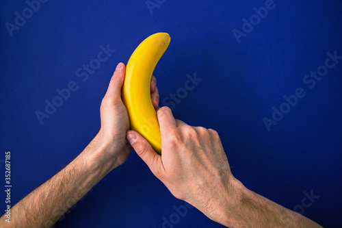 hands holding a bright yellow banana on a blue background