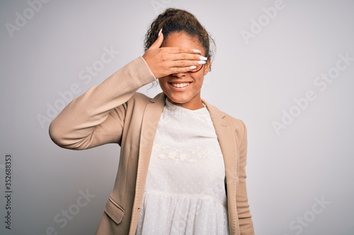 Beautiful african american businesswoman wearing jacket and glasses over white background smiling and laughing with hand on face covering eyes for surprise. Blind concept.