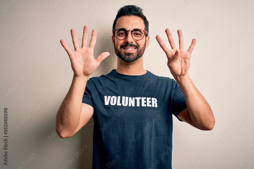 Fototapeta premium Handsome man with beard wearing t-shirt with volunteer message over white background showing and pointing up with fingers number nine while smiling confident and happy.