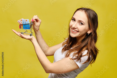 Beautiful girl in casual clothes holds a shopping trolley in the palm of her hand with bank credit cards