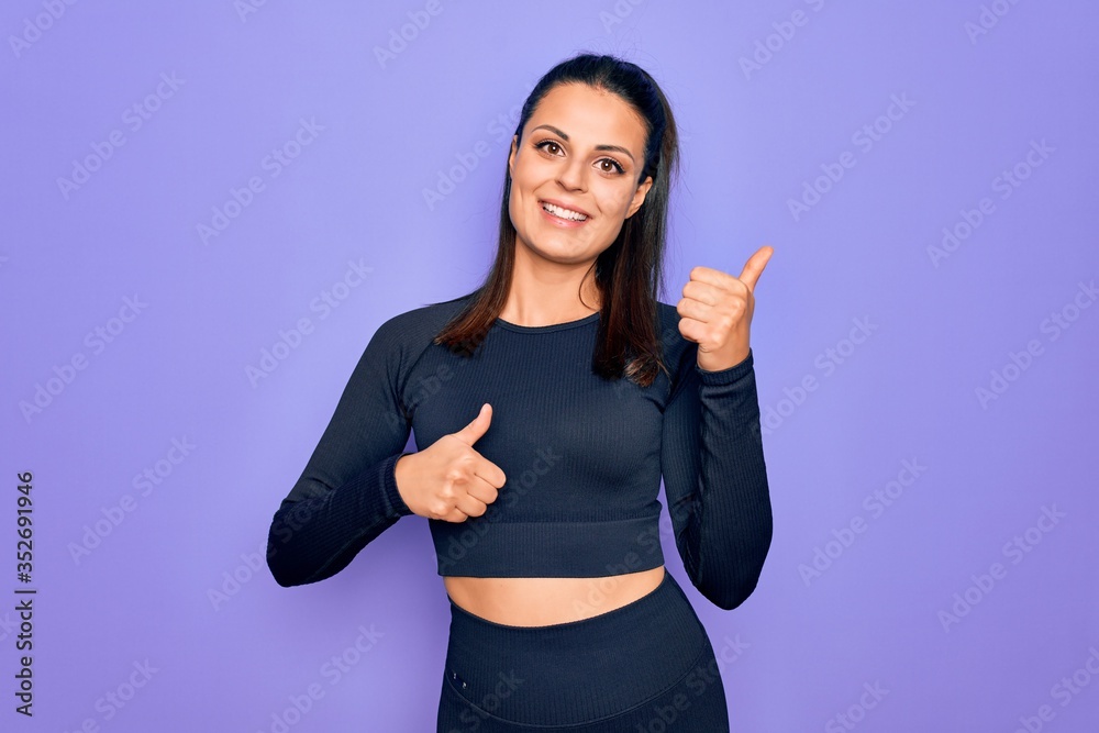 Fototapeta premium Young beautiful brunette sporty woman wearing casual sportswear over purple background Pointing to the back behind with hand and thumbs up, smiling confident