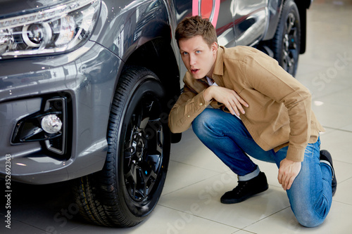 Handsome young man in casual wear checking wheels in a new car, surprised with it's perfection
