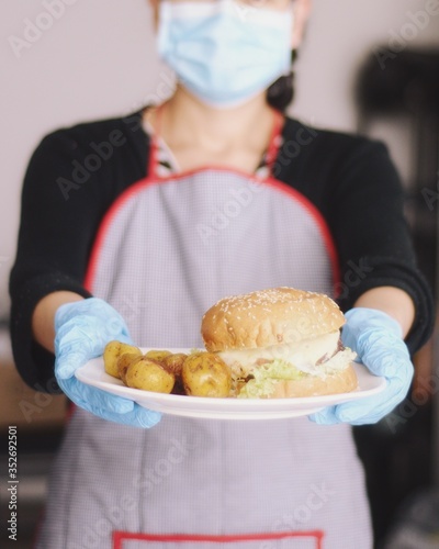 Mujer con máscara médica y guantes de goma entregando comida en su restaurante. Reapertura de negocios durante la pandemia. Compras en línea durante la Cuarentena  photo