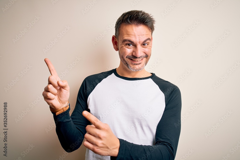 Young handsome man wearing casual t-shirt standing over isolated white background smiling and looking at the camera pointing with two hands and fingers to the side. Young handsome man wearing casual t-shirt standing over isolated white background smiling and looking at the camera pointing with two hands and fingers to the side.