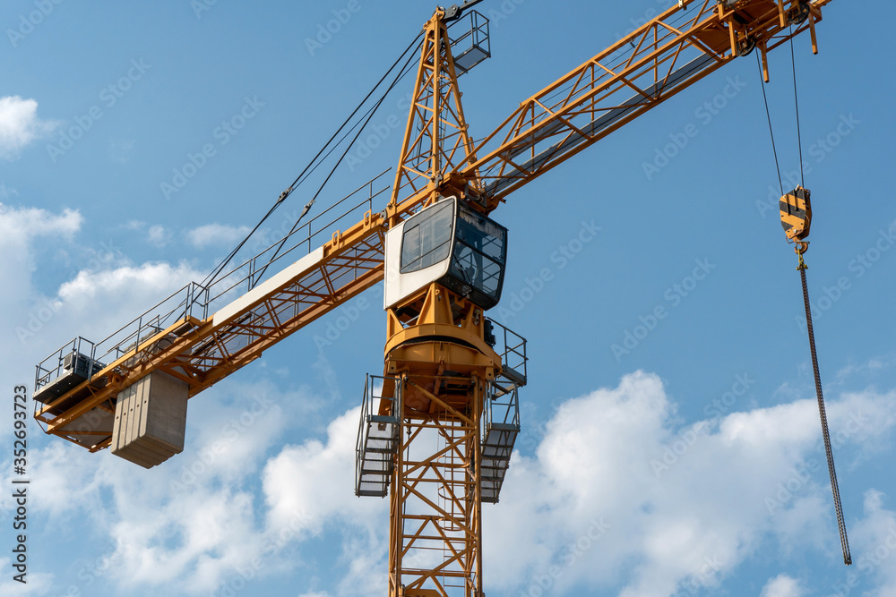 Orange tower crane against the background of a blue sky with clouds. Construction of a new brick building. Modern construction site. Housing on credit, mortgages, sale of real estate. Orange tower crane against the background of a blue sky with clouds. Construction of a new brick building. Modern construction site. Housing on credit, mortgages, sale of real estate.
