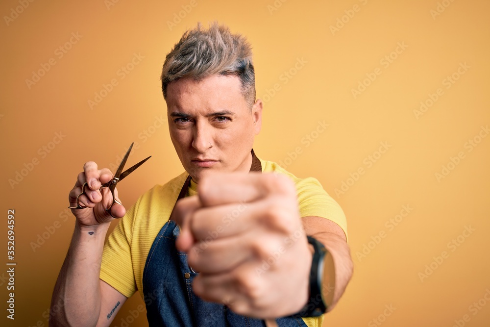 Young modern professional hairdresser man holding scissors over isolated yellow background annoyed and frustrated shouting with anger, crazy and yelling with raised hand, anger concept Young modern professional hairdresser man holding scissors over isolated yellow background annoyed and frustrated shouting with anger, crazy and yelling with raised hand, anger concept