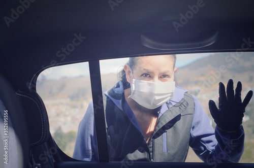 Mujer con máscara médica y guantes saluda a través de la ventana del auto desde afuera. Distancia social en la cuarentena por covid 19. photo