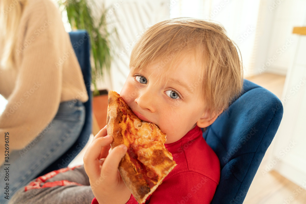Cute blonde boy eating slice of pizza.
