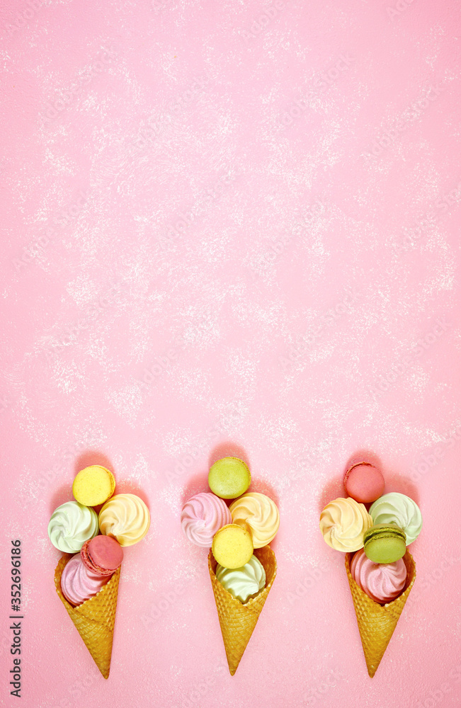 Summertime decorated border of ice cream cones filled with macarons and meringues on pink textured background, negative copy space. Stylish flat lay, top view minimalism creative layout. Vertical. Summertime decorated border of ice cream cones filled with macarons and meringues on pink textured background, negative copy space. Stylish flat lay, top view minimalism creative layout. Vertical.