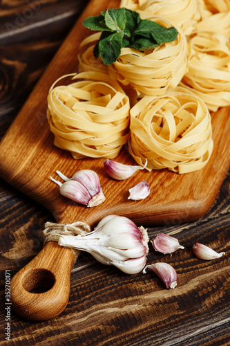 Uncooked tagliatelle nest spaghetti, garlic on a kitchen cutting board on a wooden table. Ingredients for Italian Pasta
