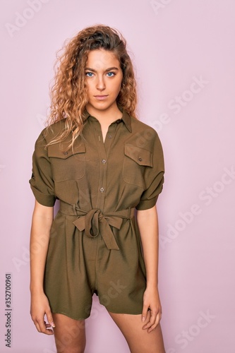 Young beautiful blonde woman with curly hair wearing casual dress standing over isolated pink background © Krakenimages.com