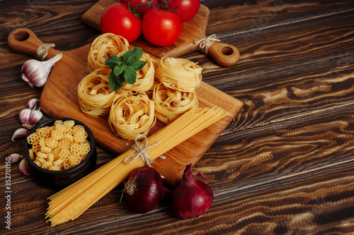 Spaghetti and fettuccine with ingredients for cooking pasta on wooden table with blank of wooden kitchen board, top view. Rustic style. Flat lay