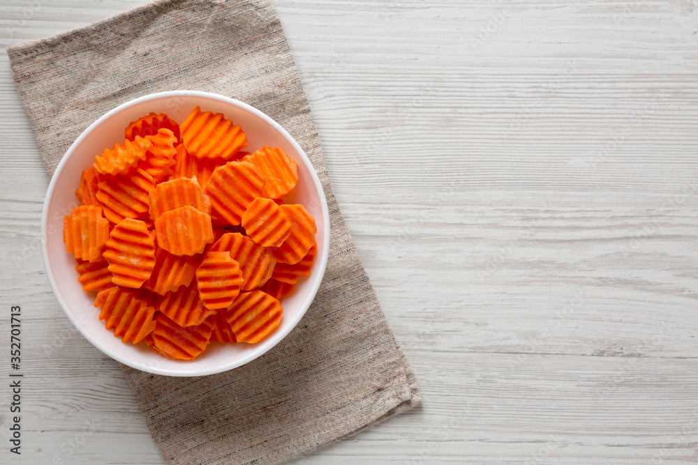 Fresh Raw Organic Carrot Chips in a white bowl on a white wooden surface, top view. From above, overhead, flat lay. Copy space. Fresh Raw Organic Carrot Chips in a white bowl on a white wooden surface, top view. From above, overhead, flat lay. Copy space.