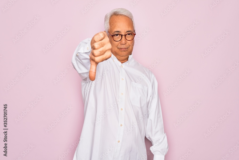 Middle age senior grey-haired man wearing glasses and business shirt over pink background looking unhappy and angry showing rejection and negative with thumbs down gesture. Bad expression. Middle age senior grey-haired man wearing glasses and business shirt over pink background looking unhappy and angry showing rejection and negative with thumbs down gesture. Bad expression.