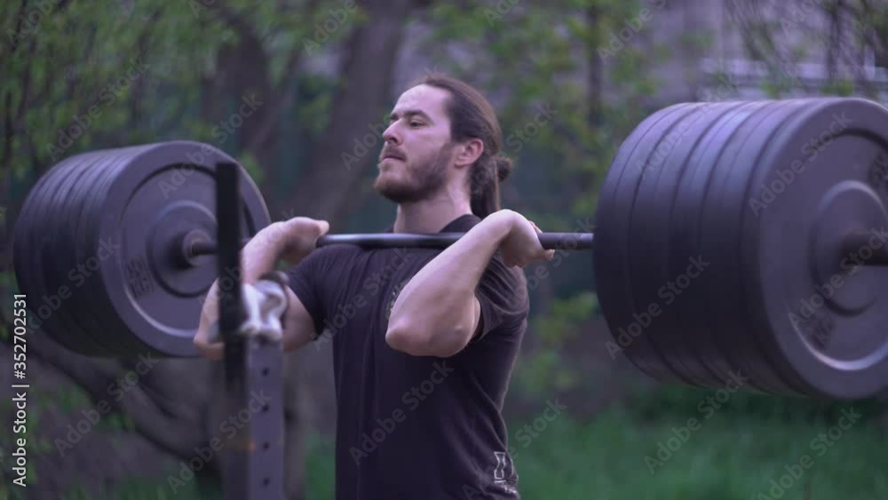 Man doing frontal barbell squats in his yard, evening workout Man doing frontal barbell squats in his yard, evening workout