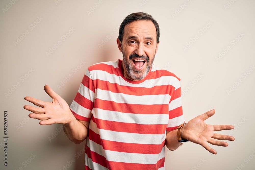 Naklejka premium Middle age hoary man wearing casual striped t-shirt standing over isolated white background clueless and confused expression with arms and hands raised. Doubt concept.