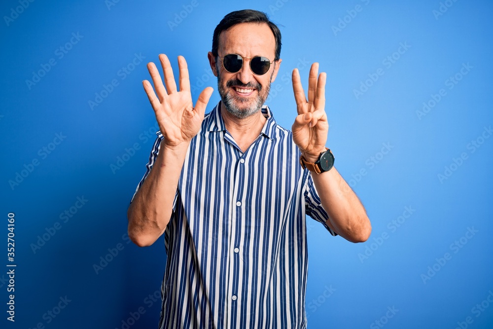 Naklejka premium Middle age hoary man wearing striped shirt and sunglasses over isolated blue background showing and pointing up with fingers number eight while smiling confident and happy.
