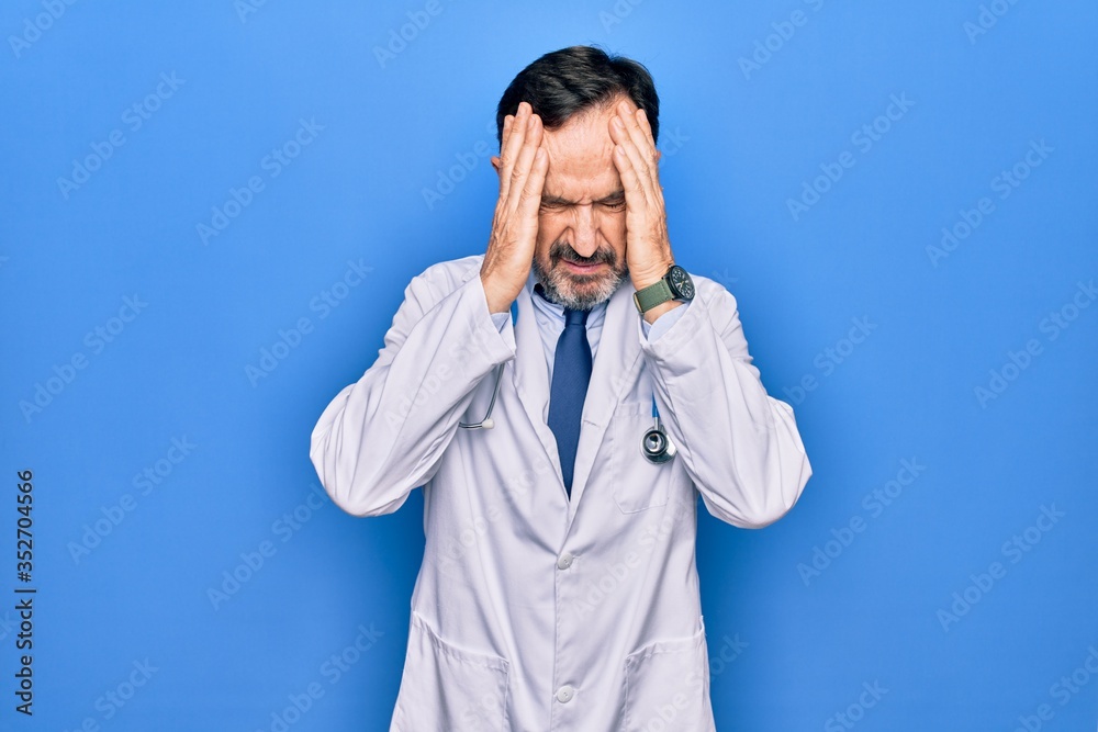 Middle age handsome doctor man wearing coat and stethoscope over isolated blue background with hand on head, headache because stress. Suffering migraine. Middle age handsome doctor man wearing coat and stethoscope over isolated blue background with hand on head, headache because stress. Suffering migraine.