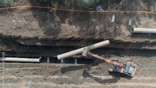 Aerial view of orange or red excavator tractor digging the sand ground to laying water pipeline installation in national infrastructure system. Outdoor construction workplace project