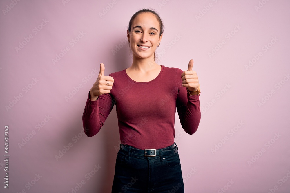 Young beautiful woman wearing casual t-shirt standing over isolated pink background success sign doing positive gesture with hand, thumbs up smiling and happy. Cheerful expression and winner gesture. Young beautiful woman wearing casual t-shirt standing over isolated pink background success sign doing positive gesture with hand, thumbs up smiling and happy. Cheerful expression and winner gesture.