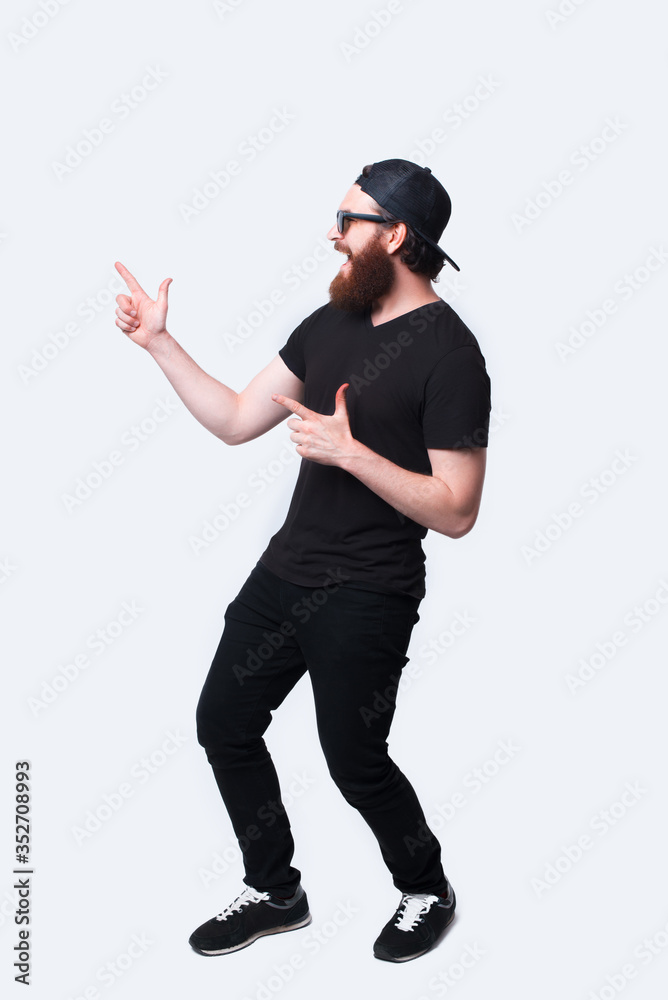Full length photo of amazed bearded hipster man pointing away Full length photo of amazed bearded hipster man pointing away