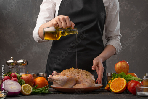 Chef pouring olive oil on a chicken preparing it for baking. Freezing in motion. Against the background of vegetables, fruits and ingredients