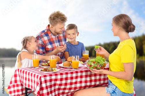 Happy family having picnic at table in park © New Africa