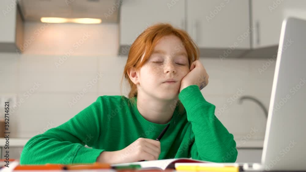Little schoolgirl falling asleep working on bored school project at kitchen Little schoolgirl falling asleep working on bored school project at kitchen