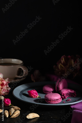 Purple macarons or macaroons cakes with cup of coffee on a black concrete background. Hard light  low key. Side view  copy space.