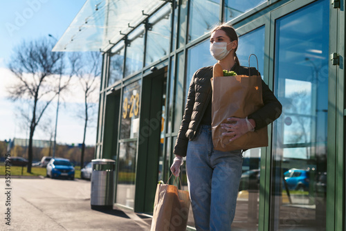 A young woman with grocery bags from a supermarket. Social distancing: face mask, disposable gloves to prevent infection and epidemic. Food shopping during quarantine