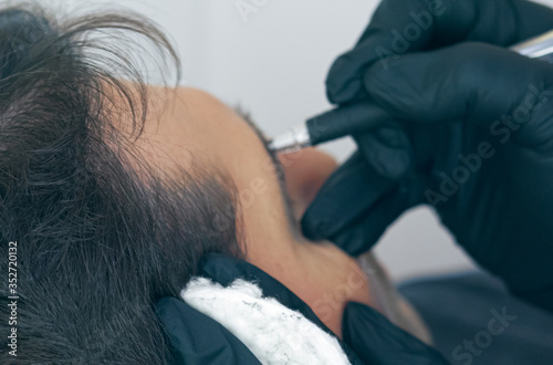 Close up of cosmetologist making permanent makeup. Microblading procedure. High quality close-up of a man laying on a couch during the esthetician brow microblading treatment.