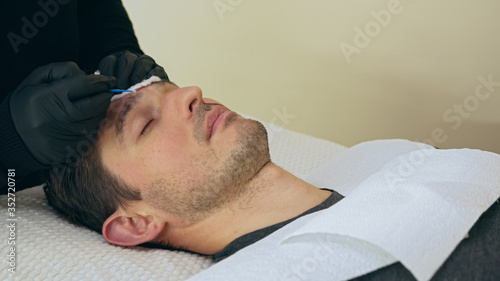 Close up of cosmetologist making permanent makeup. Microblading procedure. High quality close-up of a man laying on a couch during the esthetician brow microblading treatment.
