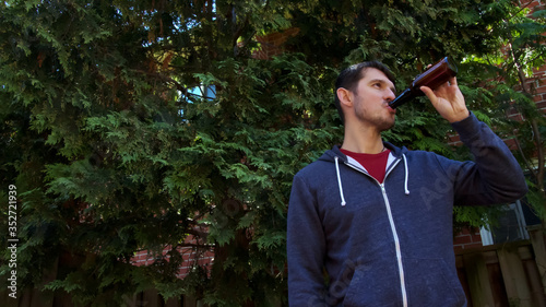High quality close-up of a young blurred man on a bright summer nature background with bottle of beer. Happy outdoor summer time. Handsome person drinking beer.