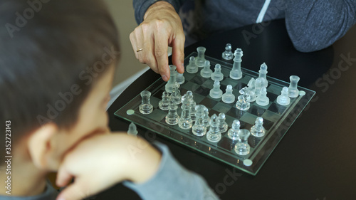High quality close-up photo of a young man playing glass chess with his little son. Father and son time together at home. Smart boy playing with daddy