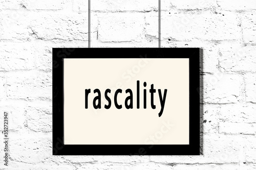 Black frame hanging on white brick wall with inscription rascality photo