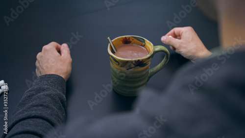 High quality close-up of a man mixing hot chocolate beverage in his cup with small white marshmallows view from the back. Handsome male drinking hot chocolate with marshmallows.