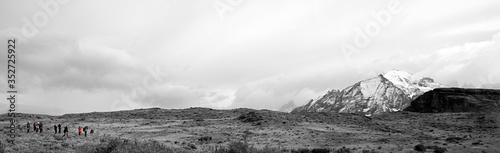 Black and white filter on Patagonia landscape. Snow capped mountains on right panning to grassy meadow with herd of Guanaco, and line of Photographers. Orange coat color splash. 