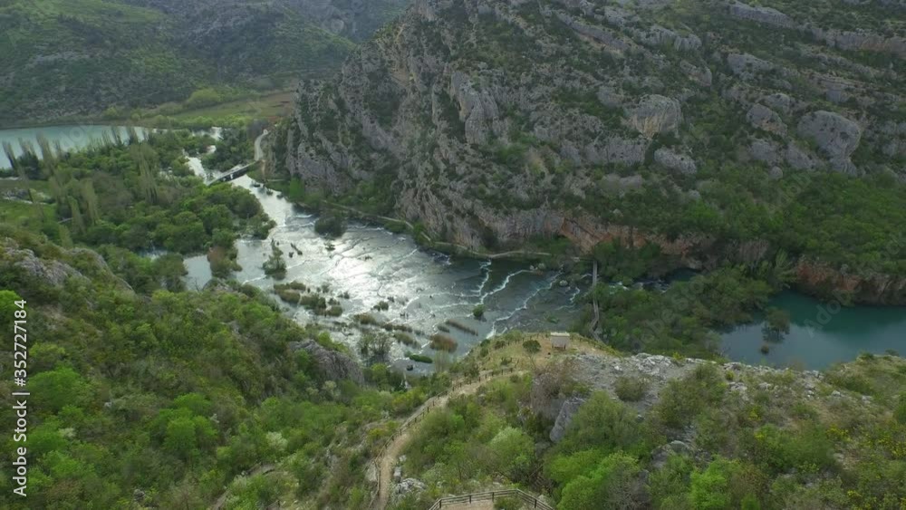 Aerial panning shot of river flowing amidst rocky mountains in valley, drone flying over plants in forest - Krka, Croatia Aerial panning shot of river flowing amidst rocky mountains in valley, drone flying over plants in forest - Krka, Croatia