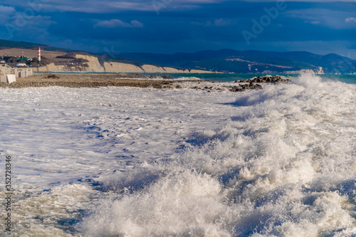 In a storm  waves in snow-white foam fall on the pebble beach of Gelendzhik. In the background Gelendzhik lighthouse and rocks