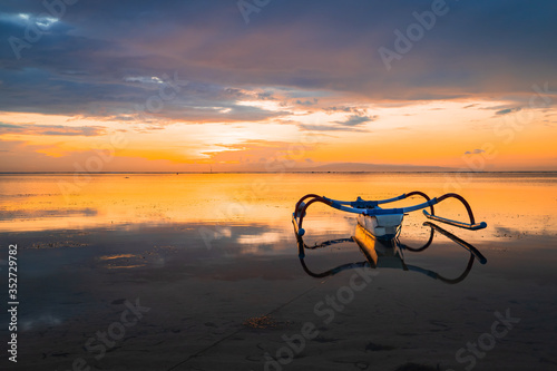 Seascape. Fisherman boat jukung. Traditional fishing boat at the beach during sunrise. Water reflection. Sanur beach, Bali, Indonesia.